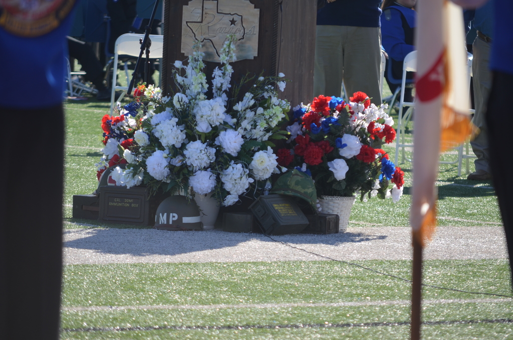 podium on football field with flowers, helmets, and ammunitions cases decorating the bottom for Veterans Day