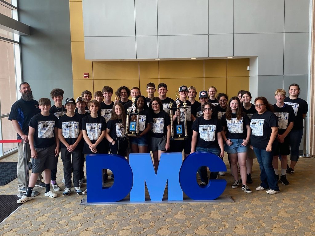 Wildcat Band students gathered with trophy behind "DMC" sign